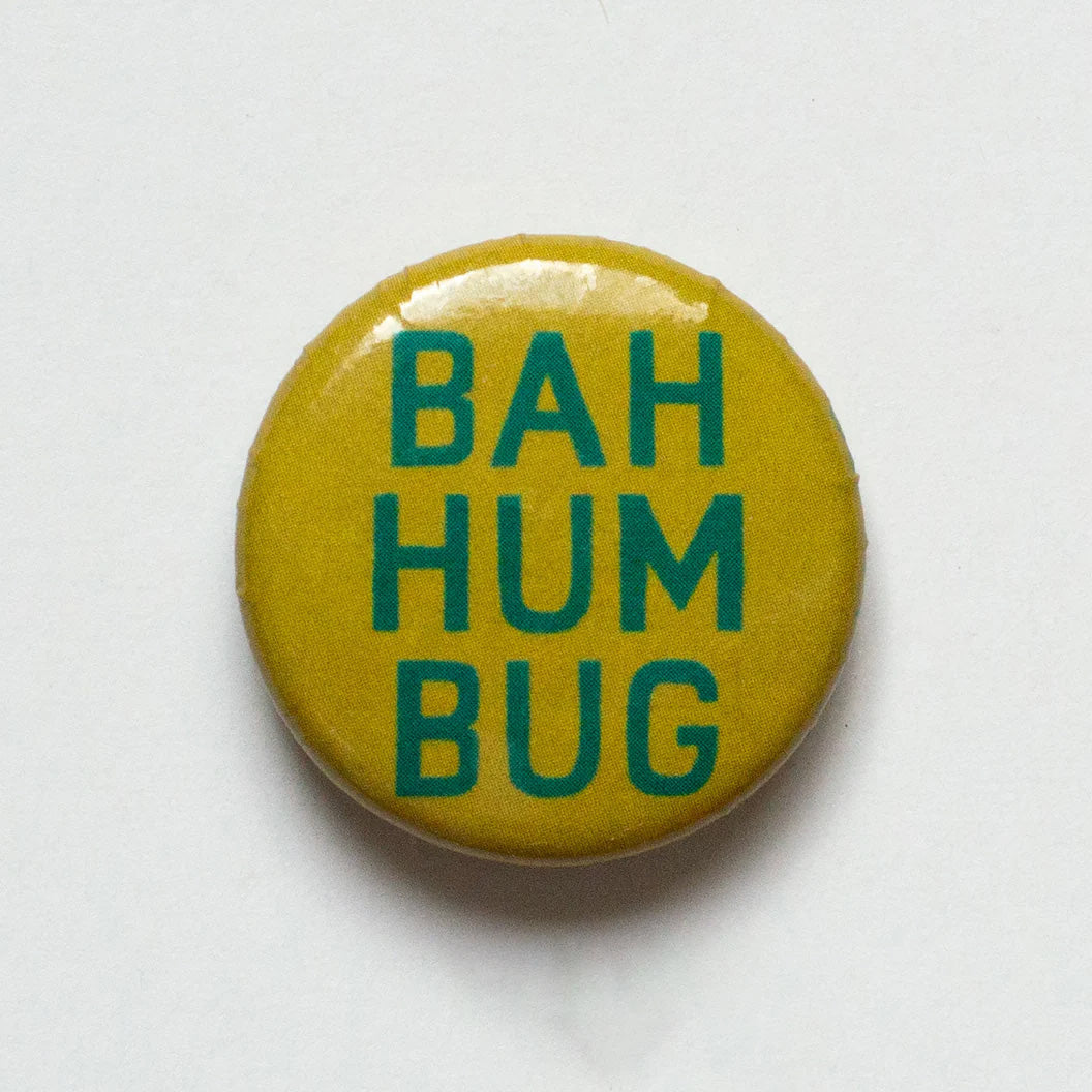 Olive Green one inch button with green lettering saying Bah Hum Bug