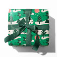 A present with forest gift wrap in green with deer, pine trees and flying owl illustrations