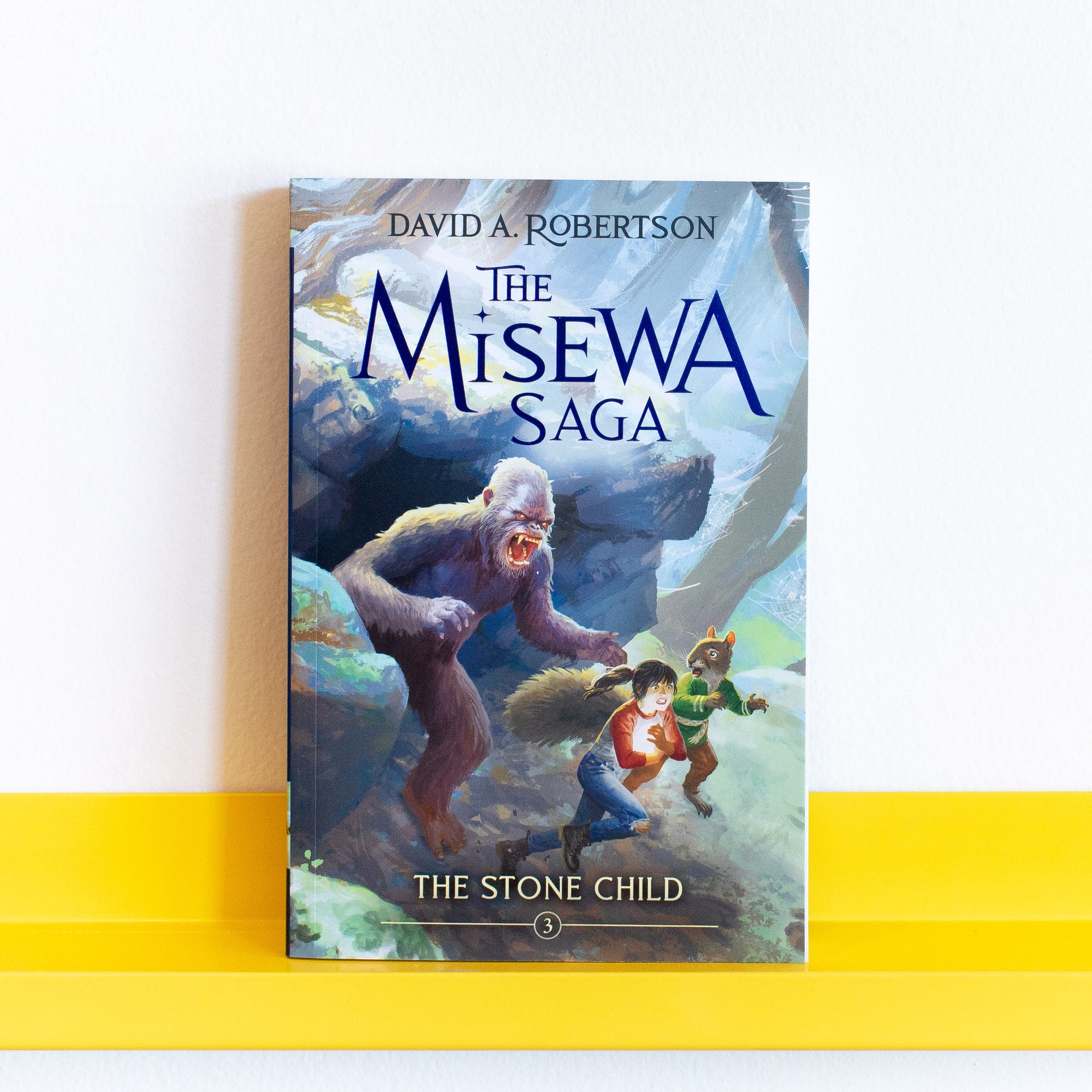 Book cover of The Stone Child: The Misewa Saga by David A. Robertson on a yellow shelf with a white background.
