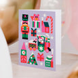 Greeting Card in lavender with colorful illustrations of holiday trees, presents, nutcracker, and a small train illustration showing a mouse driving a tiny train with sheep in back.