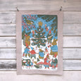 Tea towel with drawings by Phoebe Wahl of animals and people dancing and singing around a holiday tree in blues, greens, reds and white