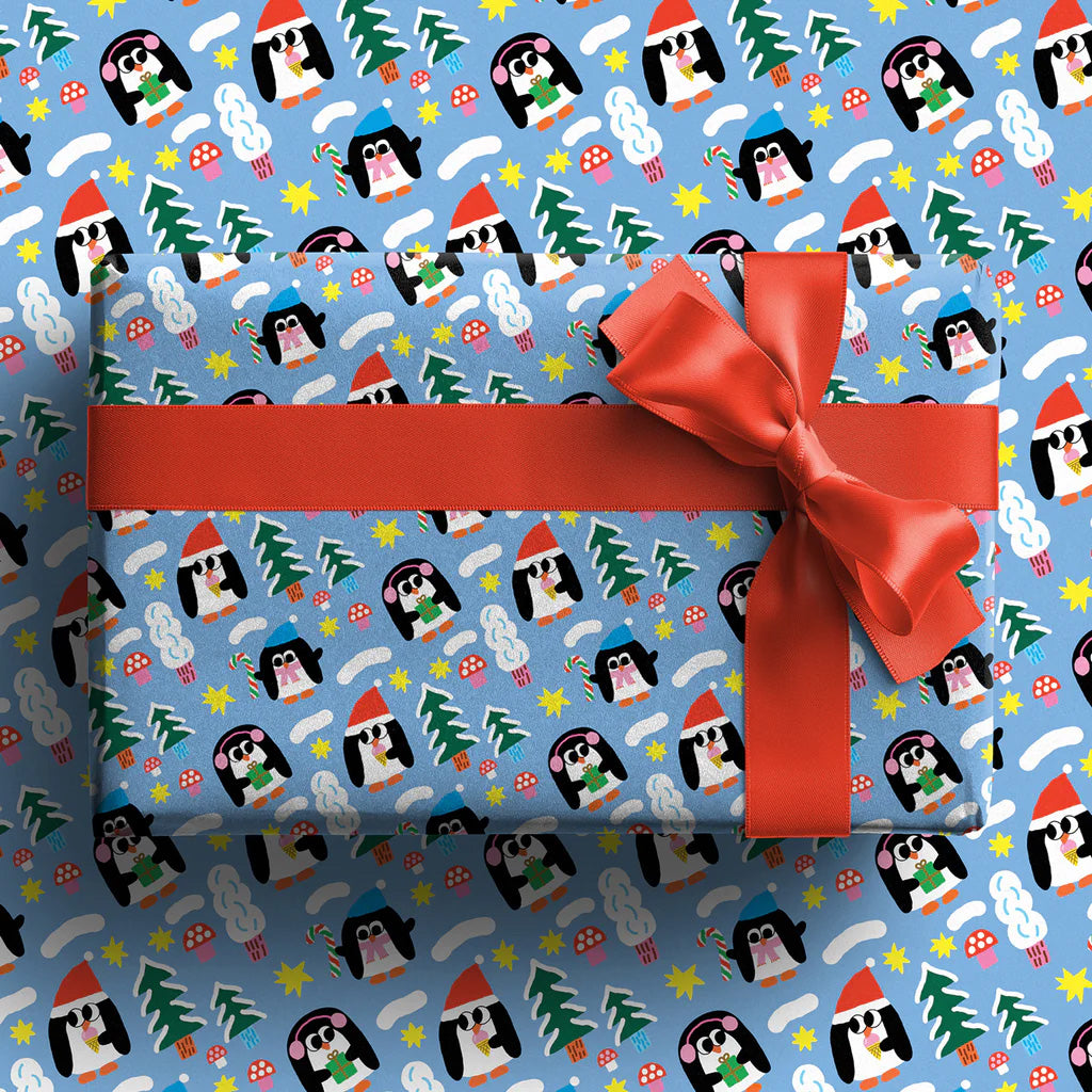 Wrapped present with a red bow showing gift wrap with illustrations of three penguins wearing winter hats and each separately holding a present, a candy cane and and an ice cream cone all on a bright blue background.