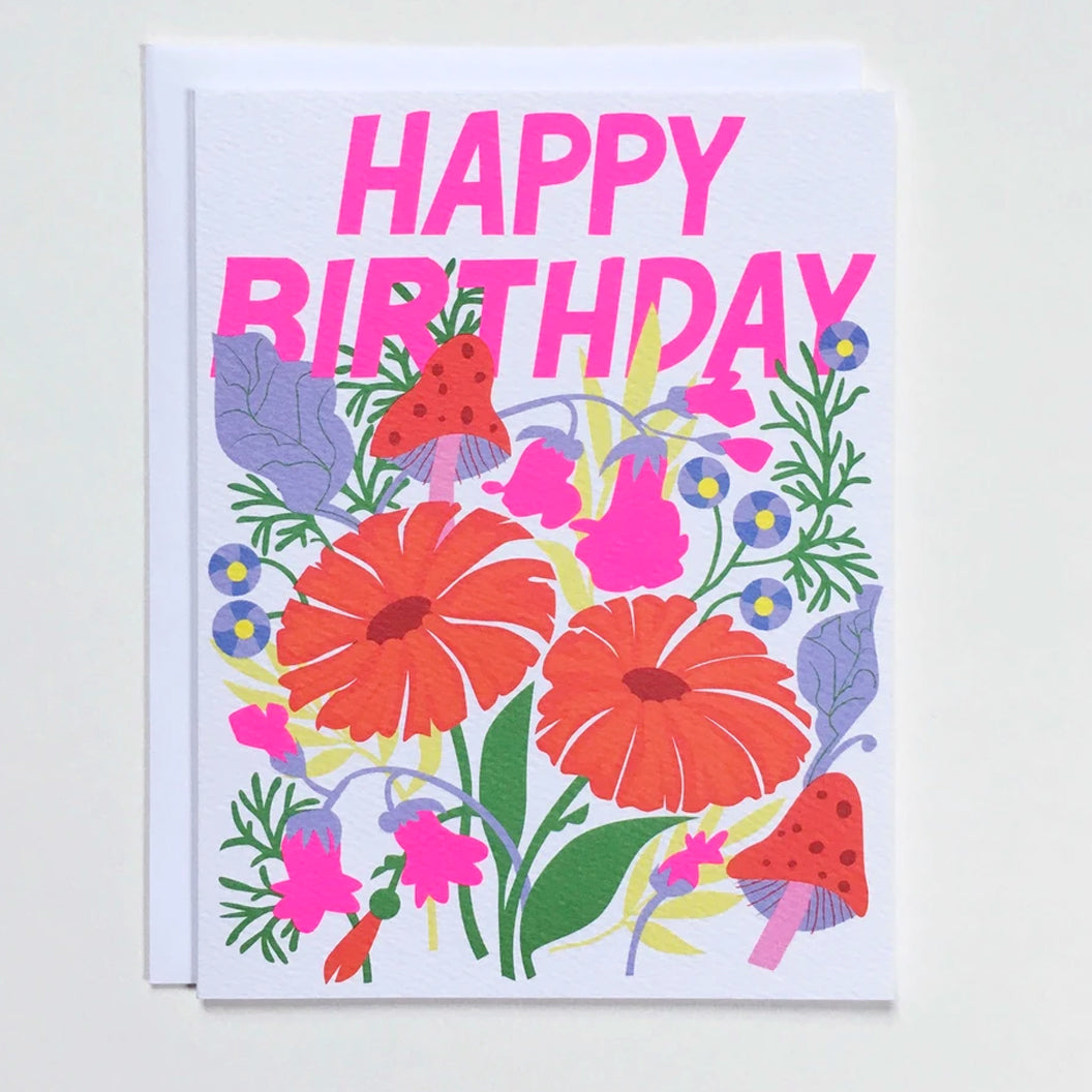 Greeting card with pink letters that say "Happy Birthday" above an illustration of mushrooms and flowers
