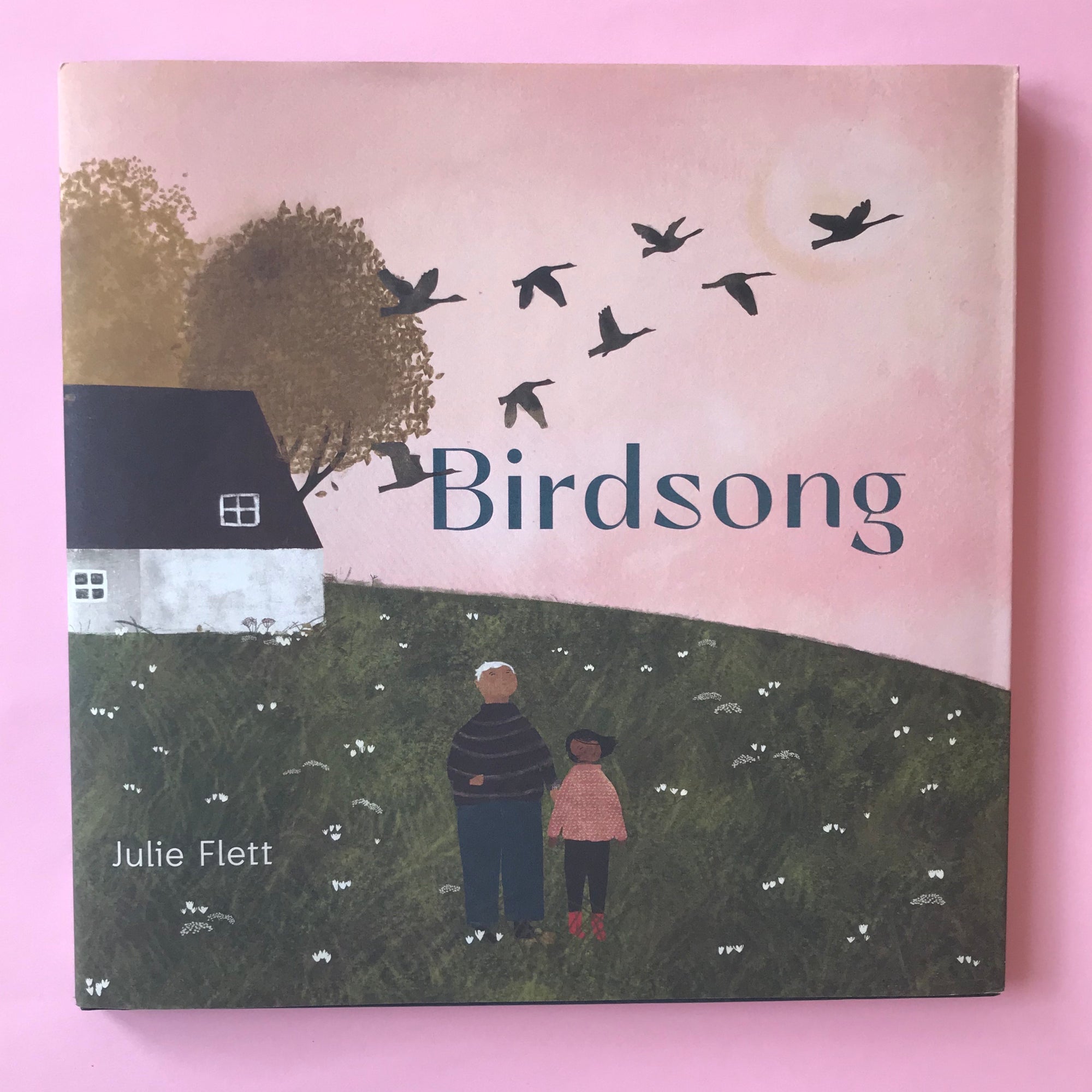 Cover of the book &#39;Birdsong&#39; by Julie Flett, depicting an illustration of an elderly woman and a young girl standing in a field, looking towards the sky with flying birds.
